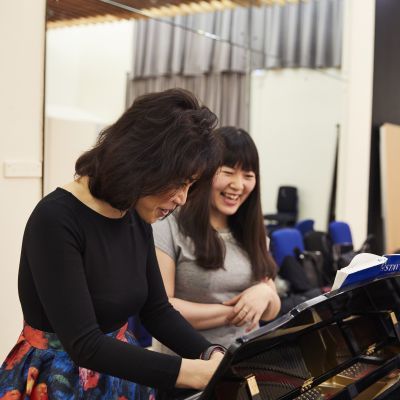 Teacher and student standing at a piano and smiling